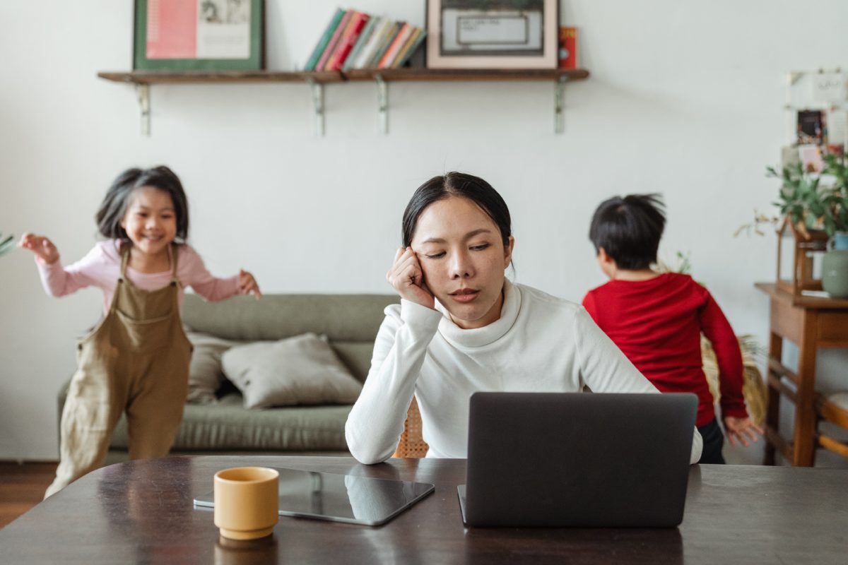 A woman working from home while her kids play behind her.